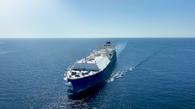 Front view of a big LNG tanker ship traveling with full speed over the calm, blue ocean