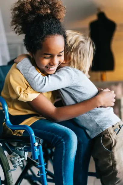 Photo of Black little girl with disability in wheelchair hugging with her younger brother.