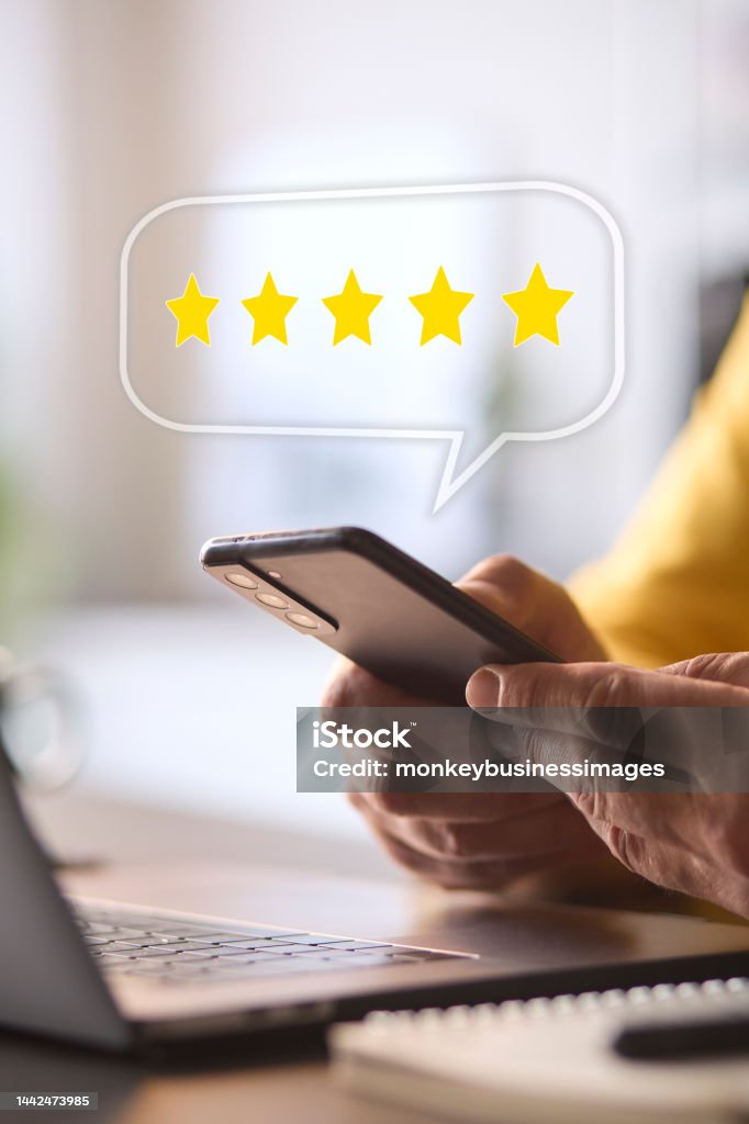 Man Using Mobile Phone With Graphic Overlay To Leave Positive 5 Star Online Review Feedback Stock Photo