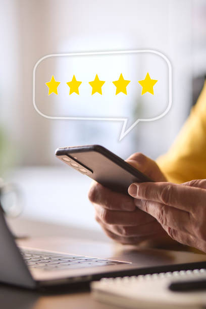 Man Using Mobile Phone With Graphic Overlay To Leave Positive 5 Star Online Review stock photo