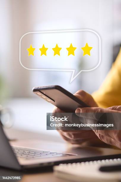 Man Using Mobile Phone With Graphic Overlay To Leave Positive 5 Star Online Review Stock Photo - Download Image Now