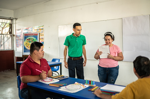 Teacher observing student psychomotor retardation teenage girl giving a presentation to classroom at school