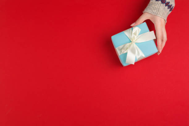 istock Female hands with christmas gift on red background, top view, copy space 1442475711