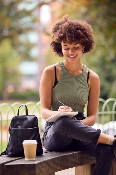 istock Young Woman Outdoors In Park Sitting On Bench Working Writing In Notebook 1442476394