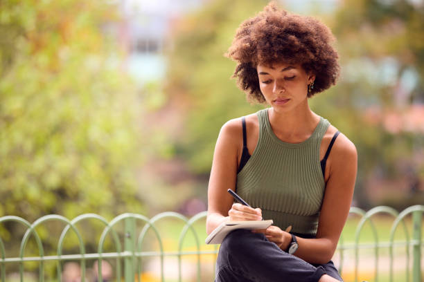 istock Young Woman Outdoors In Park Sitting On Bench Working Writing In Notebook 1442476443