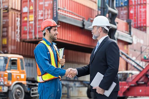 Group of male foreman or supervisor successful of their work and handshake at container yard site. Two male container yard worker handshake at container terminal yard