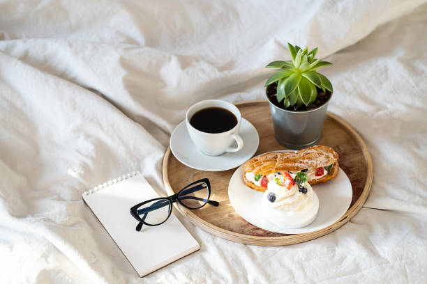 istock Cakes, coffee cup, notebook and eyeglass on wooden tray on bedding. Cozy breakfast in bed. 1442481093