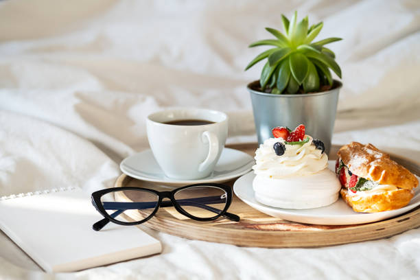 istock Cakes, coffee cup, notebook and eyeglass on wooden tray on bedding. Cozy breakfast in bed. 1442481101