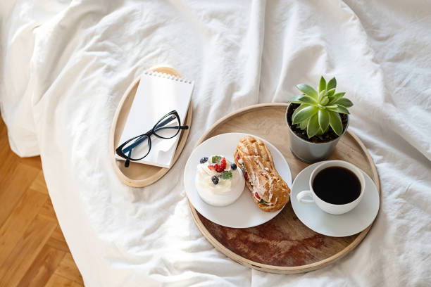 istock Cakes, coffee cup, notebook and eyeglass on wooden tray on bedding. Cozy breakfast in bed. 1442481122