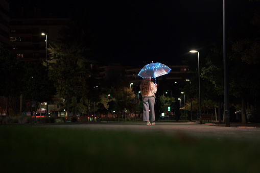 Young woman walking with umbrella with lights at night