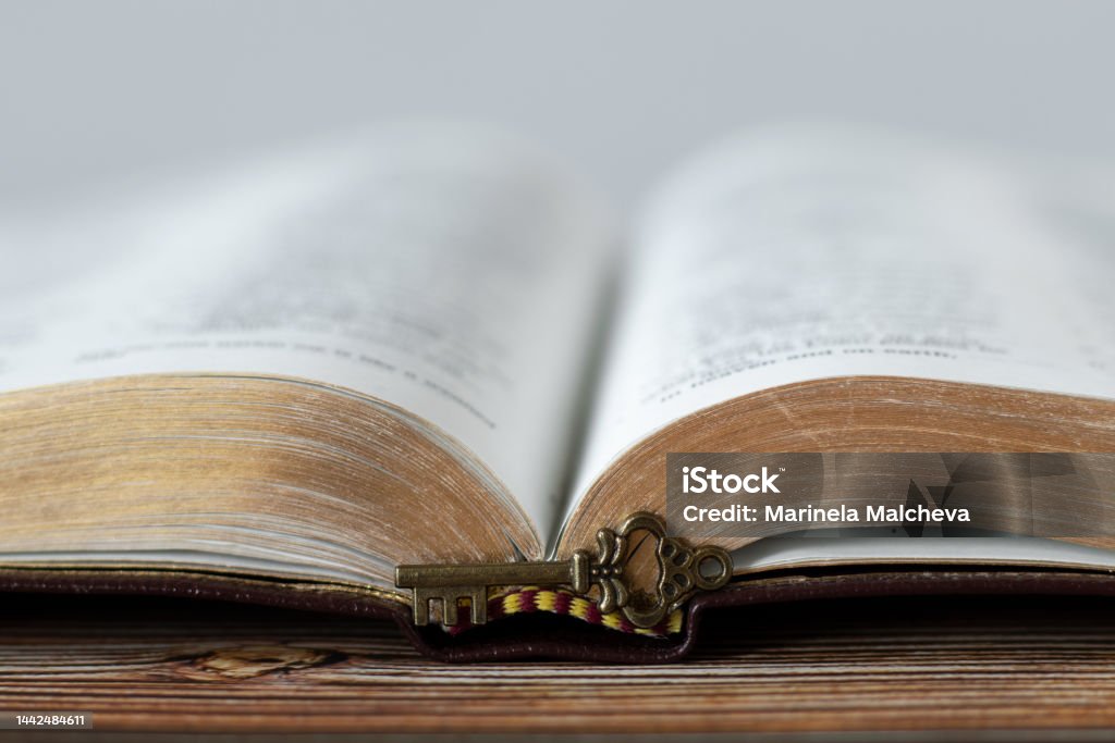 Antique key in front of open Holy Bible Book with golden pages on wooden background, close-up Antique key in front of open Holy Bible Book with golden pages on wooden background. A close-up. Christian biblical concept of revelation, prophecy, unlock mystery from Scripture. God Stock Photo