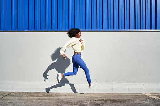 Side view of an active young woman walking and jumping with a white and blue building on the background.