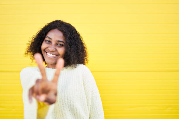 istock Young woman showing peace gesture against a yellow wall 1442486044