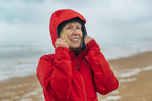 Woman in a red raincoat on the beach at Lossiemouth, Scotland, on a windy, wet, cloudy day with a pounding surf.