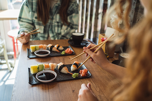 Unrecognizable woman during lunch date with her female friend using chopsticks while eating sushi