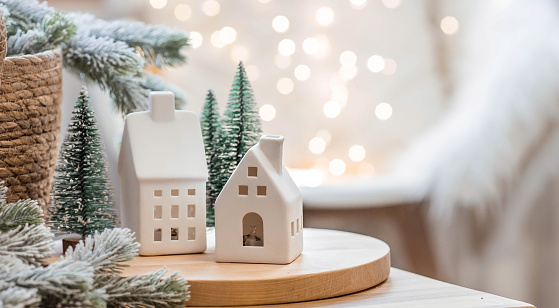 Scandinavian concept of festive decoration of the house. A bouquet of Christmas trees, a plaid in a wicker basket and Scandinavian white houses on a wooden table in the home interior of the living room.