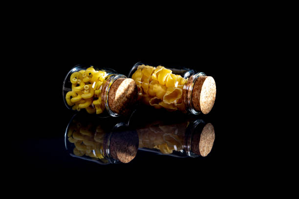 raw pasta in glass jar, wine glass. in bucket. raw pasta on black background. front view raw pasta, dropped from hand, place for text, yellow long spaghetti straws,