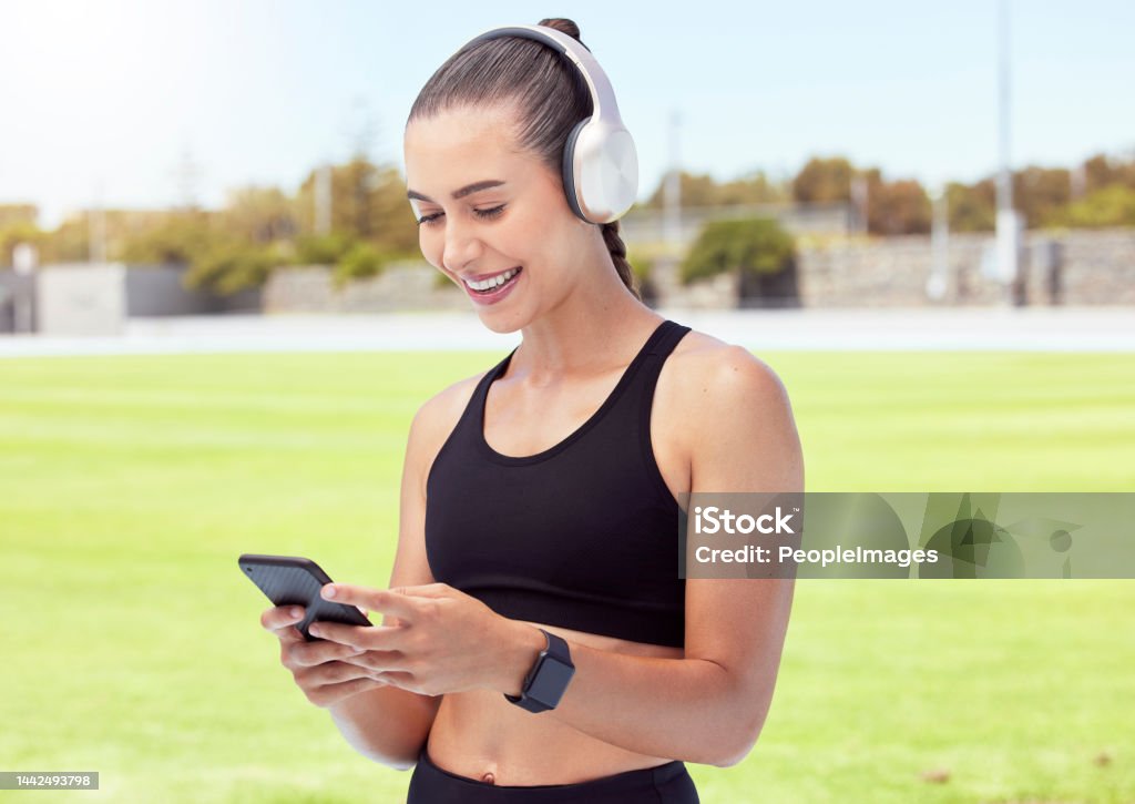 Woman athlete with phone, happy and smile with headphones and listening to music and reading a text message in the city. Young female enjoy a break from exercising outdoor and streaming audio or meme 20-24 Years Stock Photo