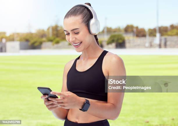Woman Athlete With Phone Happy And Smile With Headphones And Listening To Music And Reading A Text Message In The City Young Female Enjoy A Break From Exercising Outdoor And Streaming Audio Or Meme Stock Photo - Download Image Now