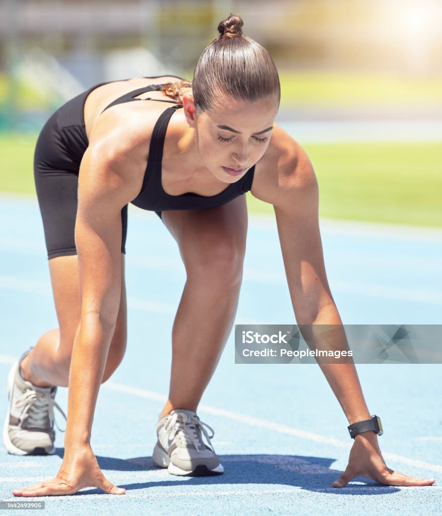 Runner, woman and focus of a athlete about to start a run on a sport track outdoor. Fitness, sports and motivation for workout training for running in a exercise for healthy living and strong cardio 20-24 Years Stock Photo
