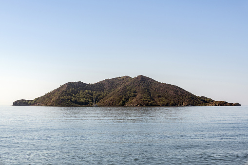 A single uninhabited island and sailing boats in the middle of the sea. This island, whose name is Kizilada, is in the Fethiye district of Turkey. Deserted island.