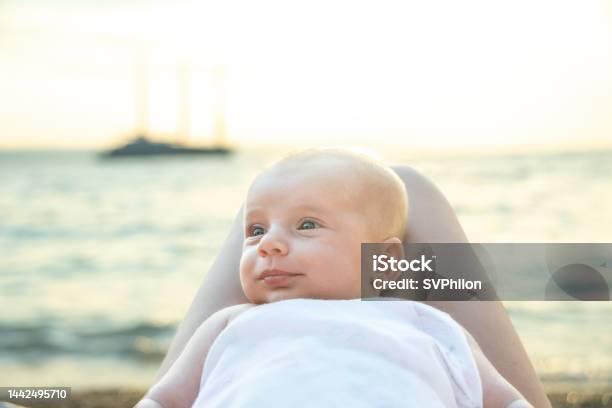 The Baby Lies On The Legs Of The Mother Near The Sea In The Evening Stock Photo - Download Image Now