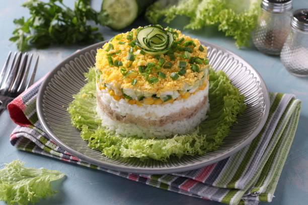 istock Festive salad with cod liver, rice, eggs, corn and cucumber on a plate on light blue background. 1442495777