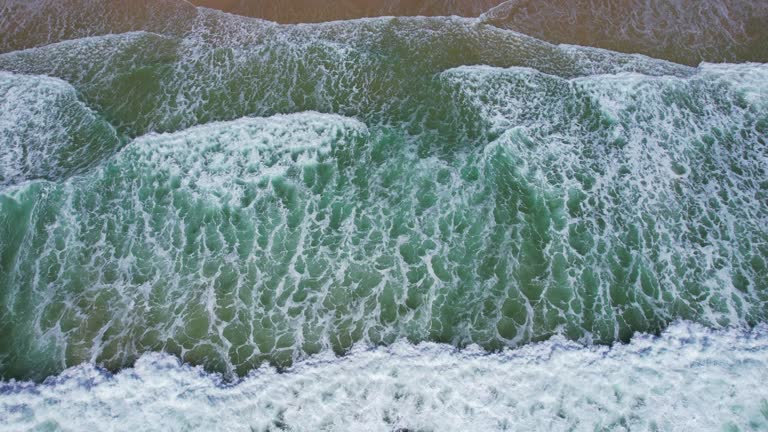 Aerial view of Pacific Ocean waves breaking on the sandy shore