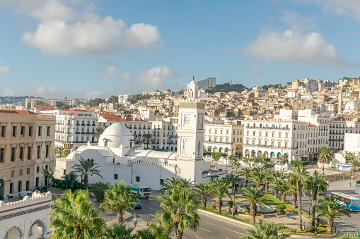 Algiers, Algeria - October 14, 2022: Djamaa el Kebir the Great Mosque of Algiers and El Aurassi Hotel. Panoramic aerial view of buildings, busses, cars and garden palm trees.