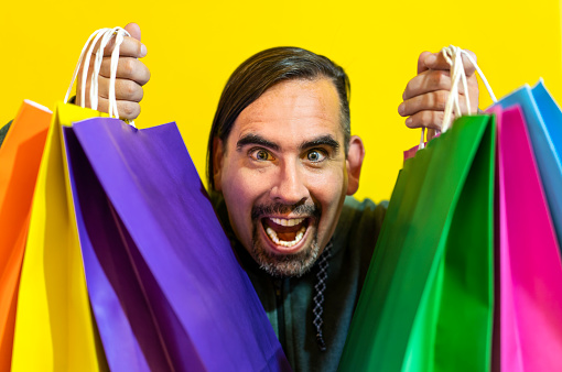 Close-up of a crazy man holding colorful shopping bags over yellow background. Shopping Concept
