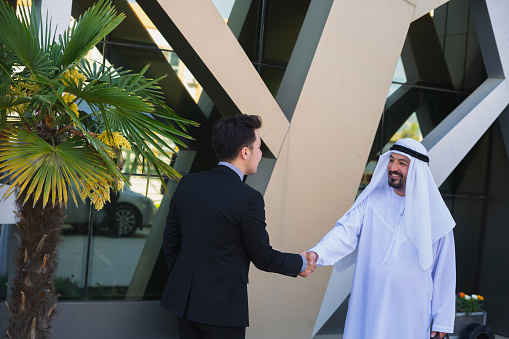 Arab and western businessmen making deal and shaking hands outdoors