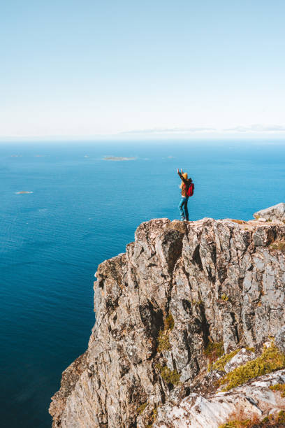 Travel in Norway woman on the edge cliff adventure active lifestyle vacations hiking outdoor aerial sea view top of mountain stock photo