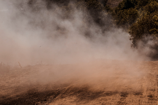 A dust storm. Powdered dust and sand flowing into air on a gravel road. Concept of extreme weather events, rally and offroad races. Copy space.