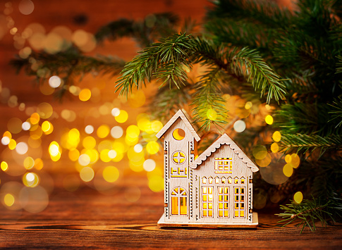 wooden house in lights under a spruce branch on a wooden background