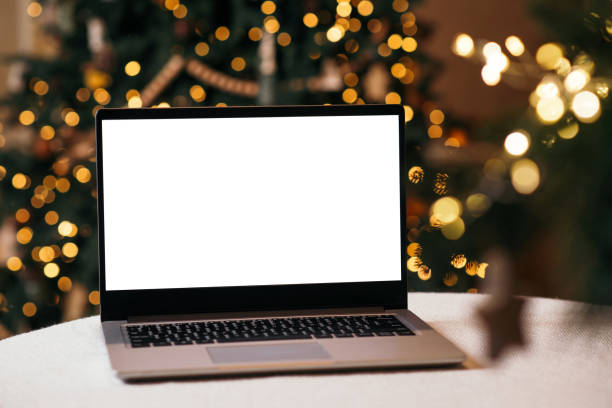 istock Front view of white screen laptop in home with christmas tree warm light. Remote work. Black Friday discounts. Online shopping. Gifts for the new year and christmas. 1442510217