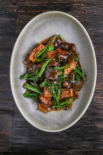 Vegan Stir-fry Tofu with broccoli vegetables, rice noodles and chili in teriyaki glaze sauce on dark wood