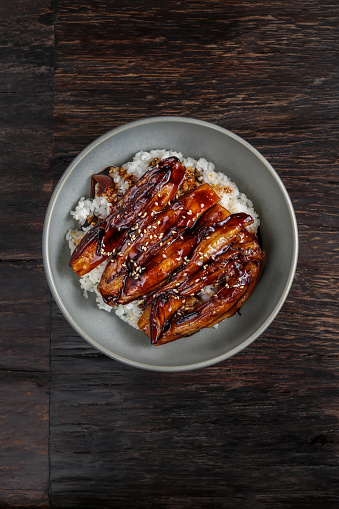Vegan Fried eggplant bowl with rice and teriyaki glaze sauce on dark wood and chopsticks
