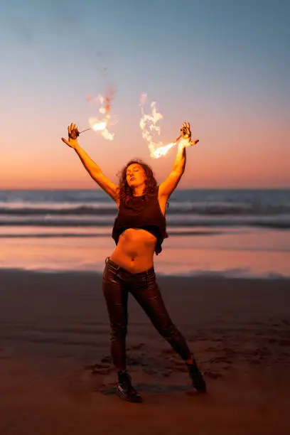 Photo of young latin woman dancing and performing with fire on the beach at sunset