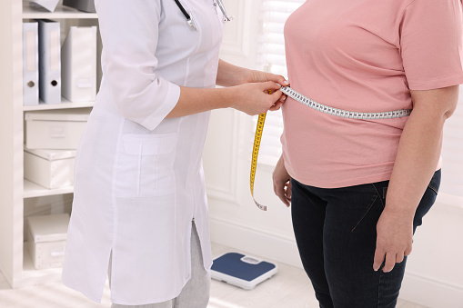 Nutricionista mide la cintura de una mujer con sobrepeso con cinta adhesiva en la clínica, primer plano photo
