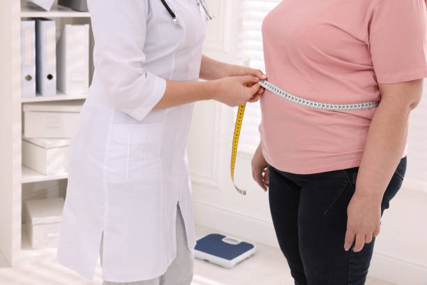 Nutritionist measuring overweight woman's waist with tape in clinic, closeup stock photo