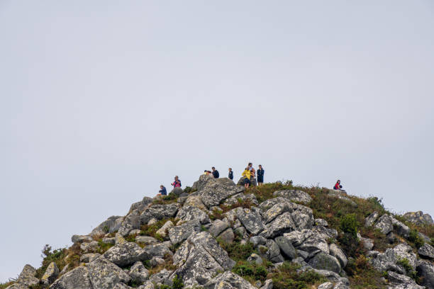 group of mountaineers and tourists on top of a rocky mountain with moss and lichen under a gray cloudy sky. people talking, looking at the landscape, taking photos and sitting on the rocks. - climbing rock climbing rock mountain climbing imagens e fotografias de stock