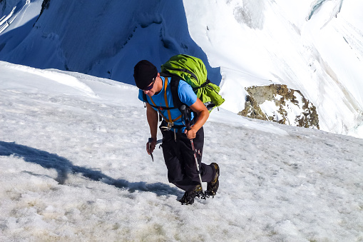 Description: Mountaineer with crampons and ice axe hiking up steep  snow field on Jungfrau with panoramic mountain scenery in the background. Jungfrau-Höhenweg, Bernese Alps, Switzerland, Europe.