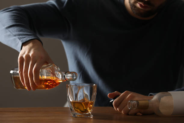 Addicted man pouring alcoholic drink into glass at wooden table indoors, closeup Addicted man pouring alcoholic drink into glass at wooden table indoors, closeup alcoholism alcohol addiction drunk stock pictures, royalty-free photos & images