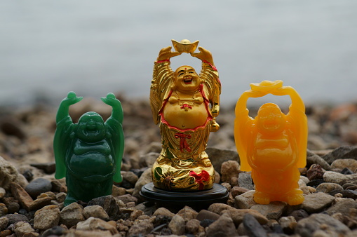 Three small Buddha figurines on the river bank. Religious symbols.