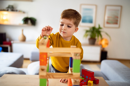 Kid girl play toys at home, kindergarten or nursery. Baby child playing playthings cubes and wood puzzle, pyramid sitting on the floor. Happy preschool education indoor. 3 years old little toddler.