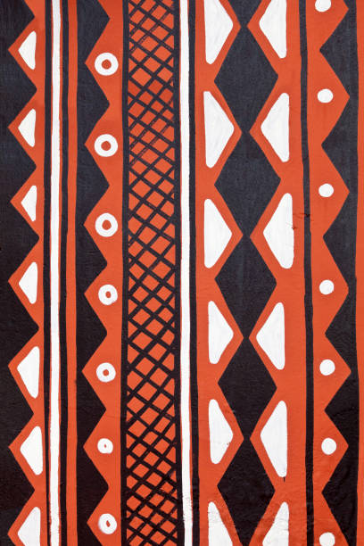 Photograph of geometric pattern in Western Africa in a naively painted style onto a roughly rendered concrete wall using a burnt sienna brown, black and white paint.