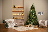 Modern Christmas living room interior in studio apartment. Large decorated Christmas tree, sofa, plaid, gift boxes, fluffy carpet, light garlands.