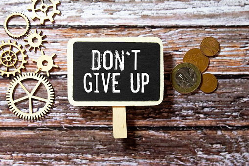 Don't Give Up text on sticker with pen on white background.