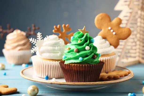 Photo of Different beautiful Christmas cupcakes on light blue wooden table