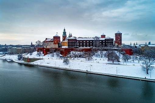 Kraków, Poland – January 14, 2021: Historic royal Wawel Castle and Cathedral in Krakow, Poland, with Vistula River, walking people, snow and promenade in winter